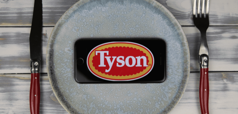 Logo da Tyson Foods exibida em celular, sobre um prato de comida.