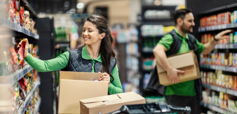 Dois trabalhadores em varejo reposicionando produtos em prateleiras.