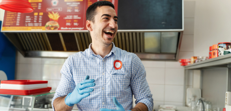 Homem trabalhando em cozinha de restaurante, sorrindo. Exemplificando as vagas de trabalho no setor alimentício.